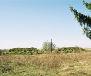 Łąka w tle krzyż i mogiły usypane z ziemi, pokryte trawą