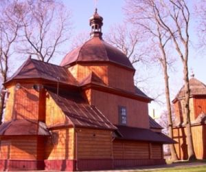 Drewniany budynek z dachem w kształcie kopuły, W oddali drugi budynek drewniany, drzewa bez liści