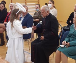 Uczennica dzieli się opłatkiem i składa życzenia ks. kanonikowi
