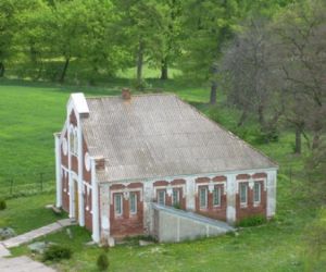 Stary budynek z cegły z białymi elementami, siwy dach, w oddali drzewa i krzewy