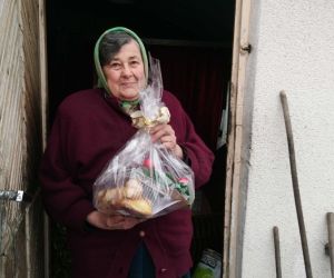 Starsza kobieta w chustce na głowie w drzwiach wejściowych do swojego domu, trzyma w rękach stroik świąteczny