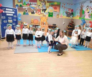 Przedszkolaki w szeregu. Na przedzie Jedna z dziewczynek recytuje, a wychowawczyni trzyma dla niej mikrofon