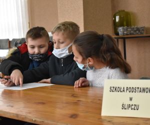 Dzieci siedzą wewnątrz budynku i rozwiązują zadania konkursowe.