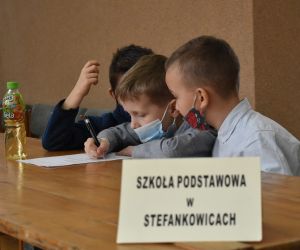 Dzieci siedzą wewnątrz budynku i rozwiązują zadania konkursowe.