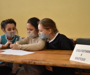 Dzieci siedzą wewnątrz budynku i rozwiązują zadania konkursowe.