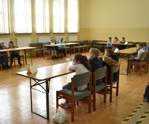 Dzieci siedzą wewnątrz budynku i rozwiązują zadania konkursowe.