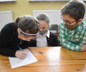 Dzieci siedzą wewnątrz budynku i rozwiązują zadania konkursowe.