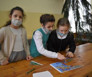 Dzieci siedzą wewnątrz budynku i rozwiązują zadania konkursowe.