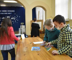 Dzieci  wewnątrz budynku rozwiązują zadania konkursowe.
