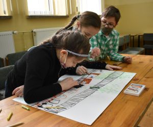 Dzieci siedzą wewnątrz budynku i rozwiązują zadania konkursowe.