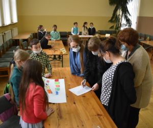 Dzieci wewnątrz budynku siedzą a Pani należące do Komisji Konkursowej przypatrują się rozwiązaniom zadania.