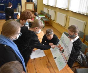 Dzieci wewnątrz budynku siedzą a Pani należące do Komisji Konkursowej przypatrują się rozwiązaniom zadania.