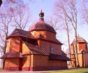 Drewniany budynek z dachem w kształcie kopuły, W oddali drugi budynek drewniany, drzewa bez liści