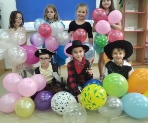 Pierwszoklasiści przebrani za postacie z bajek trzymają w dłoniach kolorowe balony