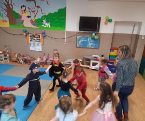 Przedszkolaki w strojach postaci z bajek tańczą w kółku z wychowawczynią