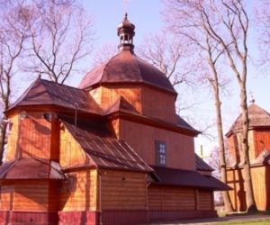 Drewniany budynek z dachem w kształcie kopuły, W oddali drugi budynek drewniany, drzewa bez liści