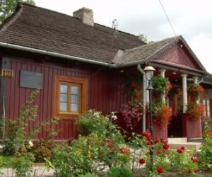 Czerwony drewniany budynek pokryty czarną dachówką, przed budynkiem rosną czerwone kwiaty