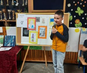 Chłopiec w granatowo-pomarańczowej bluzie prezentuje swoje prace plastyczne, wykonane różnymi metodami. Wśród nich jest portret jego mamy oraz obecnego prezydenta Ukrainy.