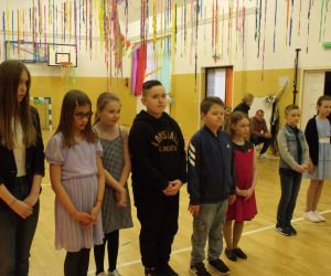 Uczniowie klasy czwartej - chłopcy i dziewczęta stoją w szeregu na przystrojonej sali gimnastycznej