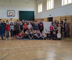 Grupowe zdjęcie uczniów i grona pedagogicznego  na tle tablicy przypominającej 79. rocznicę wybuchu powstania w getcie warszawskim