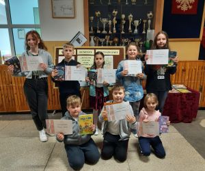 Laureaci z klas 4-8 stoją w grupie, trzymają w rękach dyplomy oraz nagrody książkowe za uczestnictwo w konkursie recytatorskim.