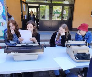 Uczniowie siedzą przy stoliku i przepisują tekst na maszynie do pisania.