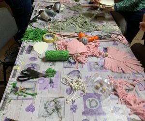 Stół na którym znajdują się nożyce, sznurek, kobiety zaplatają makramy.