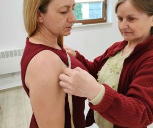 Dwie osoby wewnątrz budynku, zdejmowanie miar krawieckich.