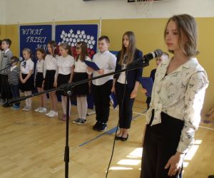 Uczennica klasy ósmej wypowiada komendę wprowadzenia sztandaru szkoły. W tle uczniowie klasy czwartej i drugiej w szeregu.