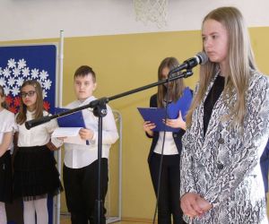 Uczennica klasy ósmej śpiewa przy mikrofonie. W tle uczniowie klasy czwartej.