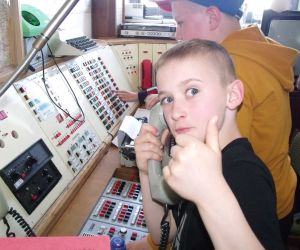 Uczeń w Muzeum Strefa Historii w Świdniku przed zabytkowym Centrum Dowodzenia, trzyma w ręku słuchawkę stacjonarnego telefonu, za nim stoi drugi uczeń