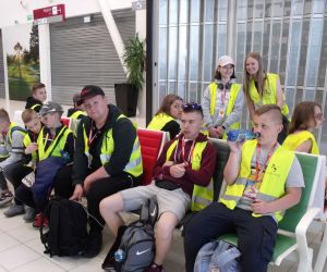 Uczniowie siedzący i stojący w poczekalni do odlotów statkami powietrznymi