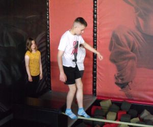 Uczniowie korzystają z atrakcji w Parku Trampolin - Akropark w Lublinie - uczeń na torze ninja, nad basenem z gąbkami, za nim stoi koleżanka