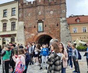 Uczniowie znajdują się przy Bramie Krakowskiej i słuchają hejnału