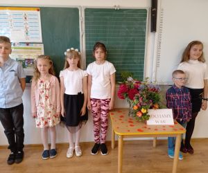 Uczniowie klasy drugiej stoją w szeregu przy stoliku. Na stoliku bukiet kwiatów.