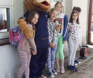 Uczniowie stoją z maskotką -sierżantem Lwem przy budynku szkolnym