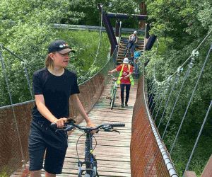 Cztery osoby prowadzą rowery po wiszącym moście.