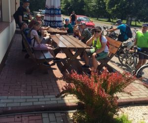 Uczniowie z nauczycielem siedzą na ławeczkach przed sklepem i jedzą lody