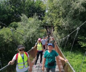 Uczniowie wraz z nauczycielem i z rowerami stoją na wiszącym moście