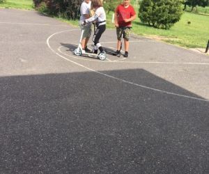 Troje uczniów stoi z hulajnogami na placu przed szkołą