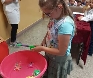 Uczennica zabawkową wędką łowi rybki, które znajdują się w misce z wodą