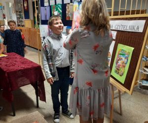 Pani bibliotekarka wielką księgą bajek pasuje ucznia na czytelnika