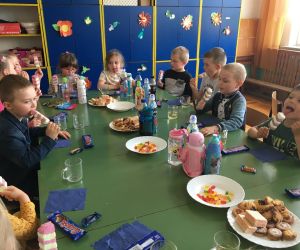 Dzieci siedzą przy stoliku ze słodkim poczęstunkiem.