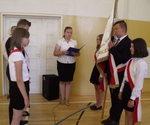 Ceremonia przekazania sztandaru szkoły - Chłopiec i dwie dziewczynki z klasy ósmej przekazują sztandar chłopcu i dwóm dziewczynkom z innych starszych klas