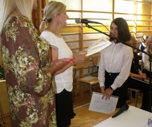 Dwie kobiety - dyrektor szkoły i wychowawczyni klasy ósmej wręczają świadectwo uczennicy klasy ósmej