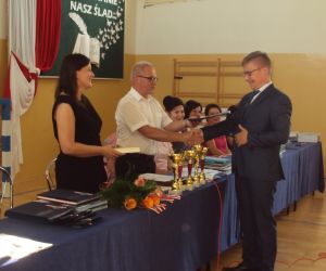 Dyrektor szkoły i wychowawczyni klasy ósmej wręczają świadectwo uczniowi klasy ósmej