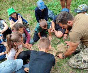 Grupa dzieci wraz z instruktorami podczas zajęć z survivalu, na świeżym powietrzu.