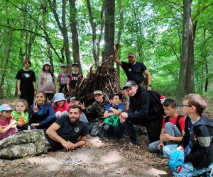 Grupa dzieci wraz z instruktorami podczas zajęć z survivalu, na świeżym powietrzu.