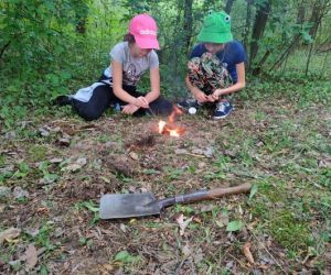 Grupa dzieci wraz z instruktorami podczas zajęć z survivalu, na świeżym powietrzu.