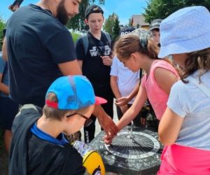 Grupa dzieci wraz z instruktorami podczas zajęć z survivalu, na świeżym powietrzu.